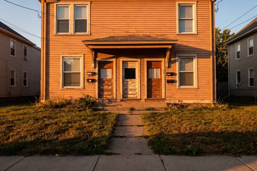 A modest triplex with three front doors, lit by a low sun
